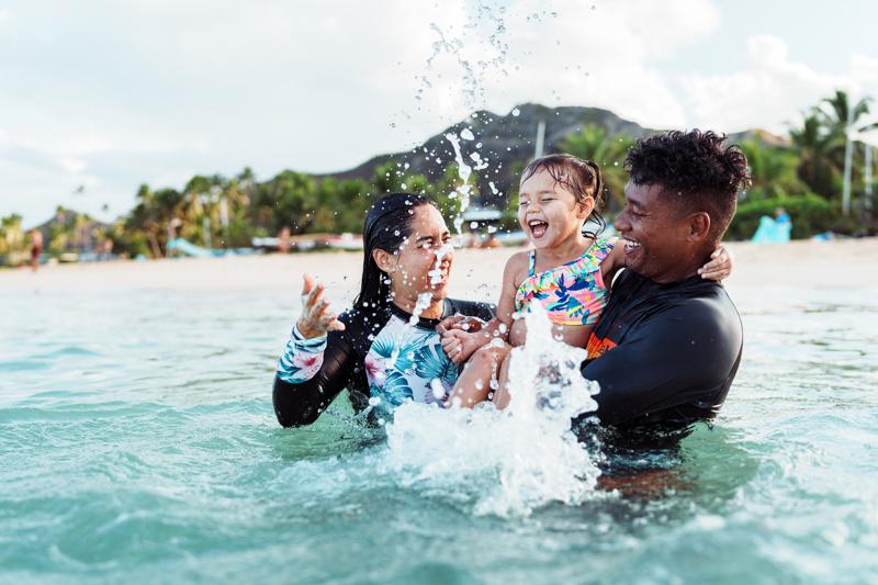 young family laughs while splashing in the ocean.