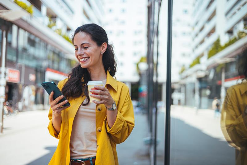 woman walking on the sidewalk at urban setting looking at phone.