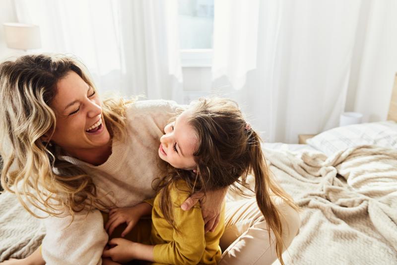 cheerful mother having fun with her daughter in bedroom