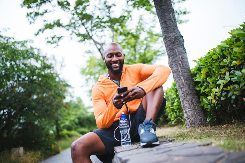 man in running shoes sitting outdoors and holding mobile phone.
