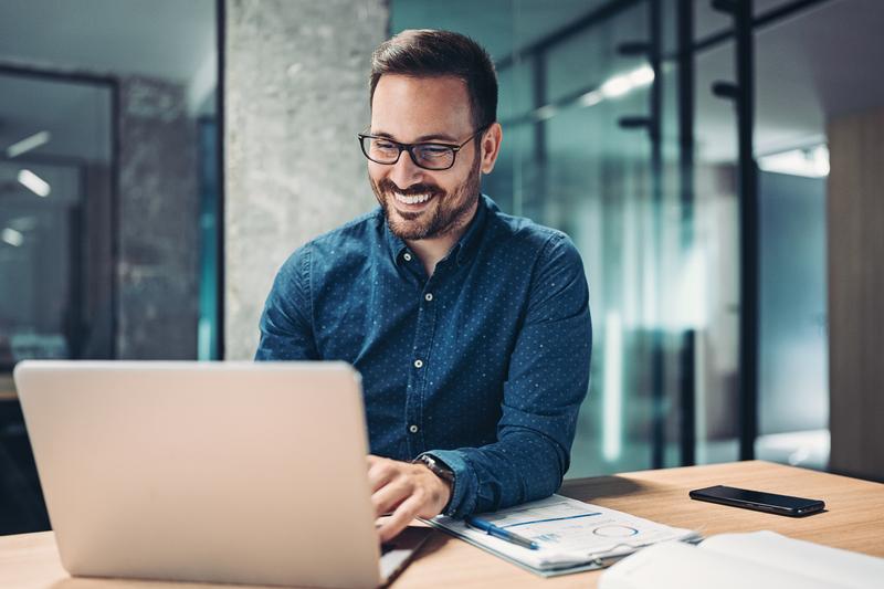 man with glasses smiling working on laptop.