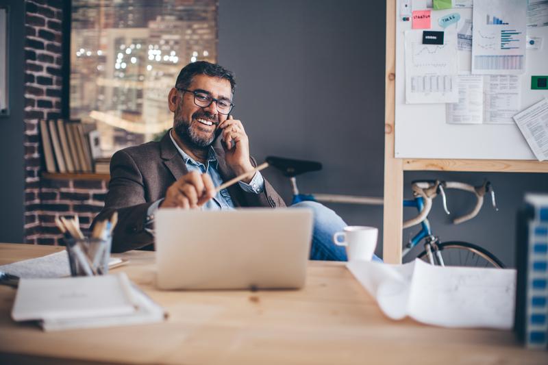 man on phone looking at laptop screen