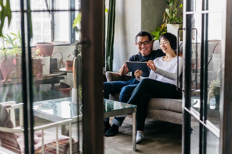 couple sitting on couch smiling looking at tablet screen