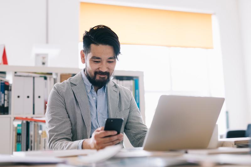 man with phone in hand and laptop open in business setting