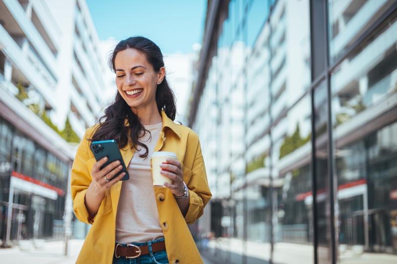 woman walking on the sidewalk at urban setting looking at phone.