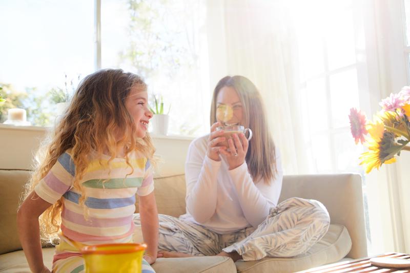 mom and young daughter sitting in their pajamas at home in the morning drinking tea and juice.