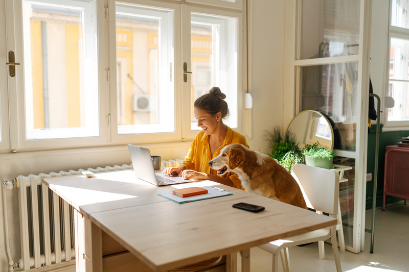 Woman sitting at a table with her dog while working on her laptop