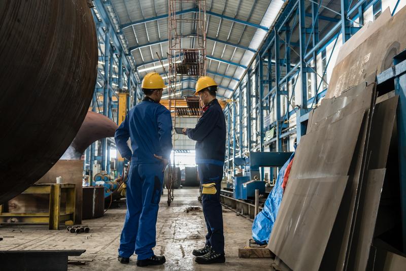 two men in hard hats having conversation in industrial setting.