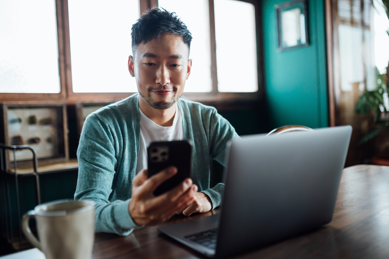 man with phone in hand and laptop open in casual setting