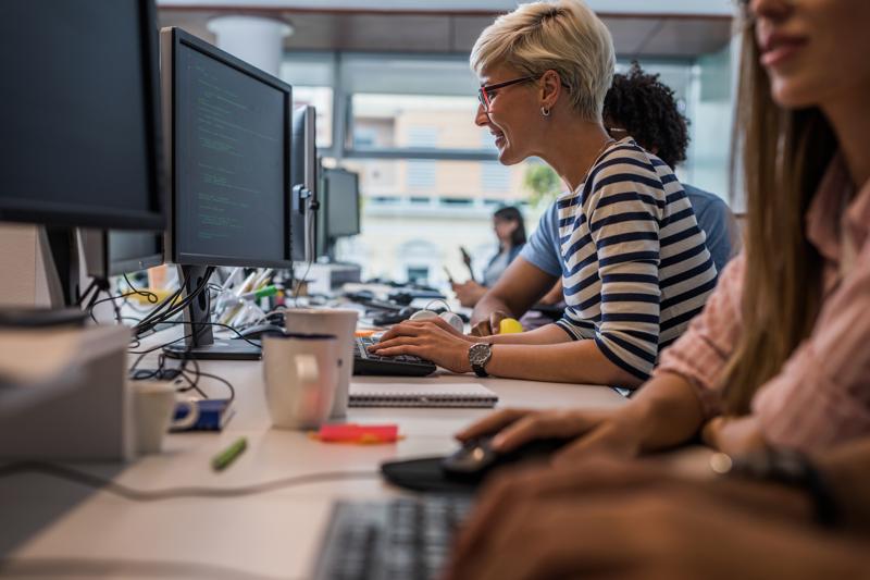 programmer coding on desktop PC in the office with her colleagues
