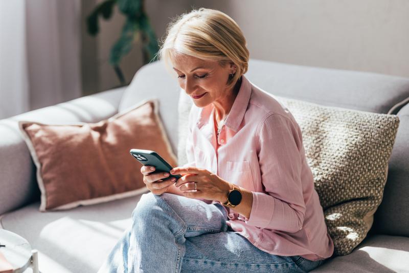 woman using her smartphone while relaxing on the cozy sofa at home