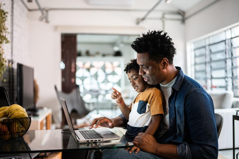 man with child on lap looking at laptop screen.